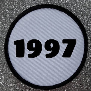 Könnte beinhalten: Runder weißer Patch mit schwarzem Rand und der Jahreszahl 1997 in Schwarz gedruckt.