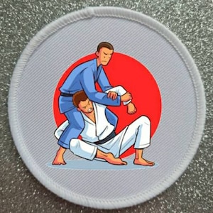 May include: A white round patch with a red circle in the center. Two figures are shown in a martial arts pose, one in a blue gi and the other in a white gi.