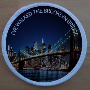 May include: A white round patch with a blue and white image of the Brooklyn Bridge at night with the text "I've walked the Brooklyn Bridge" around the edge.