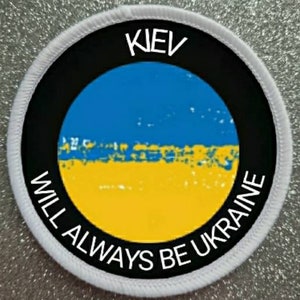 May include: Round patch with the text "KIEV WILL ALWAYS BE UKRAINE". The patch features a blue and yellow design, representing the Ukrainian flag, set against a black background. The border is white.