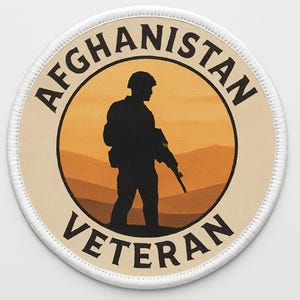 May include: Round patch with the words "AFGHANISTAN VETERAN" encircling a silhouette of a soldier against a desert landscape. The patch has a tan background with a white stitched border.