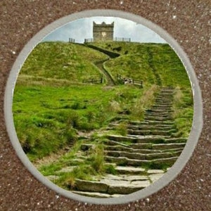 May include: A stone path leads up a grassy hill to a stone tower with a pointed roof. The path is lined with stone steps.