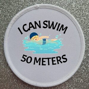 May include: White round patch with black text that reads "I can swim 50 meters". A cartoon illustration of a person swimming in a pool is above the text.