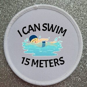 May include: White round patch with black text that reads "I can swim 15 meters". A cartoon illustration of a person swimming in a pool is shown above the text.
