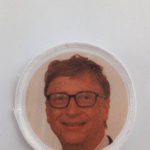 May include: A white circular patch with a stitched border featuring a color photograph of a man wearing glasses and smiling.