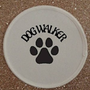 Peut inclure: Patch rond blanc avec du texte noir qui dit "DOG WALKER" et une empreinte de patte noire.