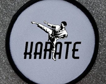 May include: A white round patch with a black border. The patch features a black and white silhouette of a person performing a karate kick. The text "KARATE" is printed in black below the silhouette.
