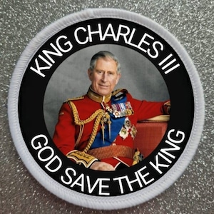 May include: A white and black circular patch with a picture of King Charles III in his royal uniform. The text around the image reads "King Charles III God Save The King".