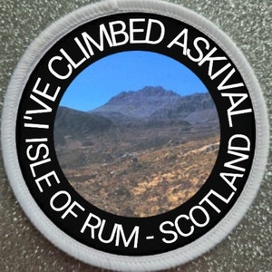 Op de afbeelding: Een ronde patch met een berglandschap. De patch heeft een zwarte rand met witte tekst: "I'VE CLIMBED ASKIVAL ISLE OF RUM - SCOTLAND". De patch heeft een witte rand.