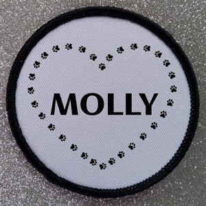 May include: White round patch with a black border. The patch has a black paw print heart design with the name "MOLLY" in the center.