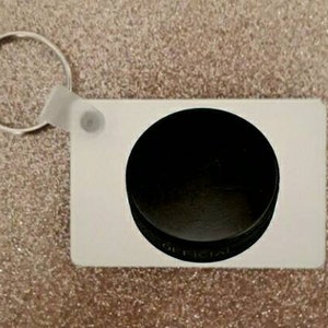 May include: White keychain with a black hockey puck design. The puck has the word "Official" printed on it.