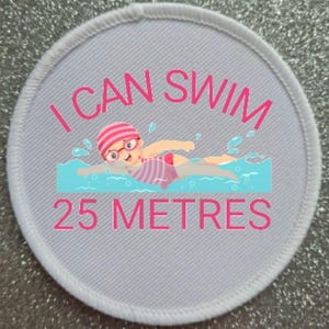 May include: White round patch with pink text that reads "I can swim 25 metres". A cartoon illustration of a girl swimming in blue water is in the center of the patch.