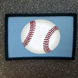Peut inclure: Une balle de baseball blanche avec des coutures rouges est affichée sur un fond bleu clair. La balle de baseball est centrée dans un cadre noir.