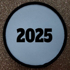 Könnte beinhalten: Runder weißer Patch mit schwarzem Rand und der Jahreszahl 2025 in Schwarz gedruckt.