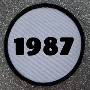 Peut inclure: Patch rond blanc avec une bordure noire et l'année 1987 imprimée en noir.