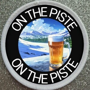 May include: Circular patch with the text "ON THE PISTE" in white. The centre shows a beer mug on a snowy landscape with mountains. The patch has a black border and a white stitched edge.