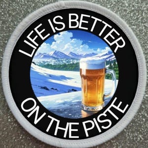 Könnte beinhalten: Ein weißer runder Patch mit schwarzem Text, der "Life is better on the piste" lautet, und ein schwarzer Kreis mit einer schneebedeckten Berglandschaft und einem Glas Bier im Vordergrund.