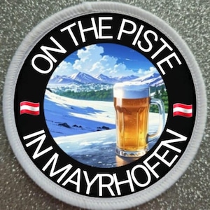 Könnte beinhalten: Ein weißer runder Patch mit schwarzem Text, der "On the Piste in Mayrhofen" lautet. Der Patch zeigt ein Cartoon-Bild einer verschneiten Berglandschaft mit einem Glas Bier im Vordergrund. Die österreichische Flagge befindet sich auf beiden Seiten des Textes.