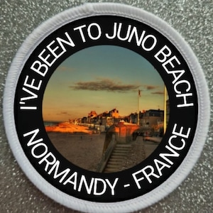 May include: A white and black round patch with the text "I've Been To Juno Beach - Normandy - France" and a photo of a beach town at sunset.