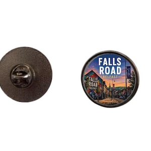 May include: A round pin with a Falls Road Belfast design. The pin features a colorful street scene with the text "FALLS ROAD BELFAST". The pin has a dark metal backing with a pin clasp.