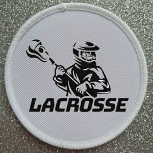 May include: White round patch with a black lacrosse player holding a stick and the word "LACROSSE" printed below.