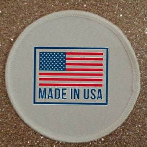 Könnte beinhalten: Ein weißer runder Patch mit einem blauen Rand und dem Text "MADE IN USA" in blauen Buchstaben. Innerhalb des Randes befindet sich eine rot-weiß-blaue amerikanische Flagge.