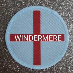 May include: A white round patch with a red cross and the word "WINDERMERE" in red letters.