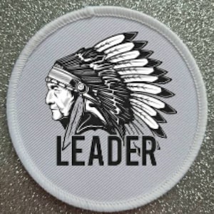 May include: White round patch featuring a black and white illustration of a Native American chief wearing a headdress. The text "LEADER" is printed below the illustration.
