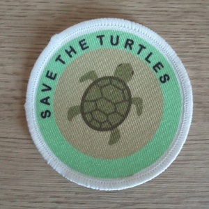 May include: A white, round patch with a green border and the text "Save the Turtles" in black. A green sea turtle is in the centre of the patch.