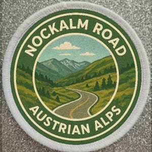 Puede incluir: Parche circular con borde verde y blanco. El parche presenta una ilustración escénica de una carretera sinuosa a través de los Alpes austriacos, con el texto "NOCKALM ROAD" y "AUSTRIAN ALPS" en letras blancas.