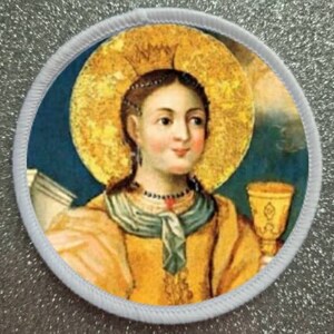May include: A round embroidered patch depicting a painting of a woman in a yellow dress and blue scarf holding a golden chalice. She has a halo and a crown on her head. The background is blue with a gold halo.