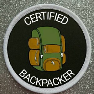 May include: A white round patch with a black background and white text. The text reads "CERTIFIED BACKPACKER". A cartoon green and brown backpack is in the centre of the patch.