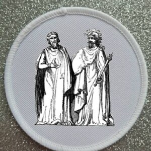 May include: A circular patch featuring a black and white illustration of two robed figures. The figures, with beards and crowns, stand against a light gray background, surrounded by a white stitched border. The patch is likely for clothing or accessories.
