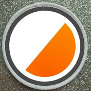 以下が含まれることがあります： 黒の縁取りのある白とオレンジの丸いパッチ。オレンジの部分は半円形です。