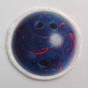 May include: A round, white-edged patch featuring a blue and red bowling ball design. The bowling ball has three black holes.