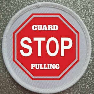 May include: White round patch with a red octagon stop sign that says "GUARD STOP PULLING" in white text.