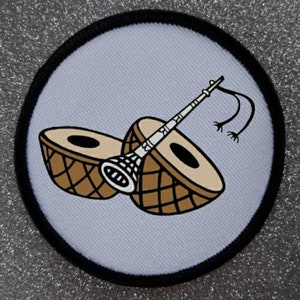 May include: A white fabric patch with a black border, featuring a brown and white illustration of two drums and a flute. The flute is decorated with a white and black design.