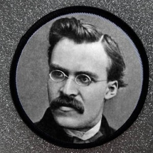 Könnte beinhalten: Schwarzweißfoto eines Mannes mit Schnurrbart und Brille. Er trägt einen dunklen Anzug und hat einen ernsten Gesichtsausdruck.