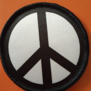 Może przedstawiać: Okrągła łatka w kolorze czarno-białym z czarnym symbolem pokoju. Łatka jest okrągła i ma białe tło z czarnym symbolem pokoju w środku.