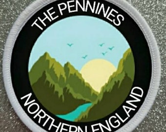 Peut inclure: Écusson rond avec une bordure noire et des coutures blanches. L'écusson représente un paysage avec des montagnes, une rivière et un soleil. Le texte "THE PENNINES NORTHERN ENGLAND" est en blanc.