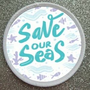 Op de afbeelding: Ronde witte patch met een blauw en wit ontwerp. De patch heeft de tekst "Save Our Seas" in blauwe letters.