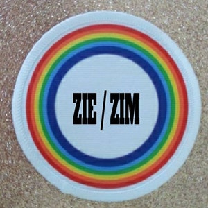 May include: White round patch with a rainbow border and the text "ZIE/ZIM" in black.