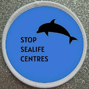 May include: A white circular patch with a blue background and a black silhouette of a dolphin jumping out of the water. The text "STOP SEALIFE CENTRES" is printed in black below the dolphin.