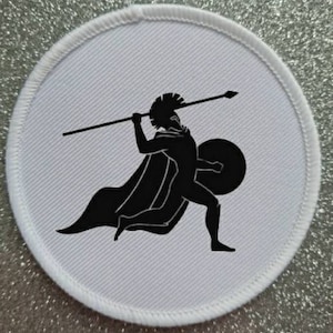 May include: A white round patch featuring a black silhouette of a warrior holding a spear and shield.