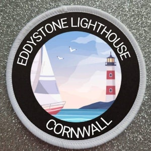 May include: A white and black round patch with the text "Eddystone Lighthouse Cornwall" around the edge. The center of the patch features a colorful illustration of a lighthouse, a sailboat, and seagulls against a blue sky.