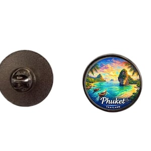 May include: A round pin with a detailed image of a tropical beach scene with the text "Phuket Thailand". The pin has a black metal backing with a pin clasp.