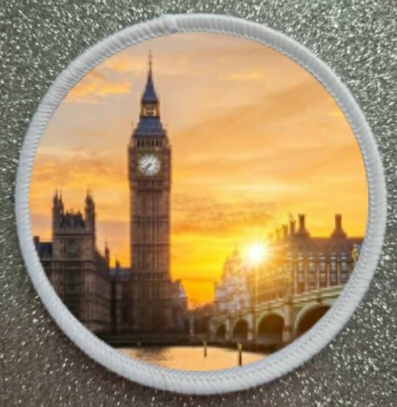 K&ouml;nnte beinhalten: Ein runder Patch mit wei&szlig;em Rand, der ein farbenfrohes Bild von Big Ben und den Houses of Parliament in London, England, zeigt. Das Bild zeigt einen Sonnenuntergang &uuml;ber der Stadt mit einem goldenen Himmel.