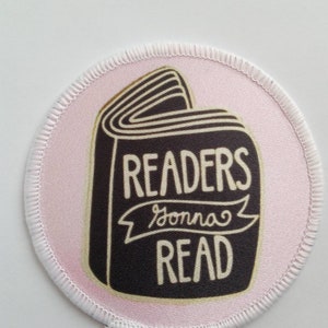 May include: A pink and white round patch with a black book illustration. The book has the text "READERS gonna READ" on it.