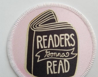 Puede incluir: Un parche redondo rosa y blanco con una ilustración de libro negro. El libro tiene el texto "READERS gonna READ".