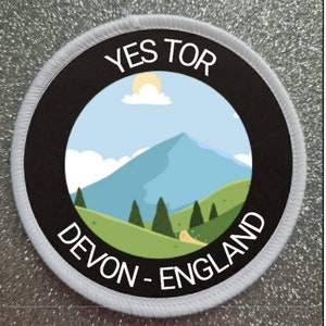 May include: White round patch with black border and a cartoon illustration of a mountain range with a sun and clouds. The text "YES TOR DEVON - ENGLAND" is written around the image.